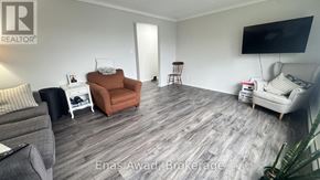 Ottawa triplex for rent - A living room with a grey couch, a brown armchair, a white side table, and a television on the wall.