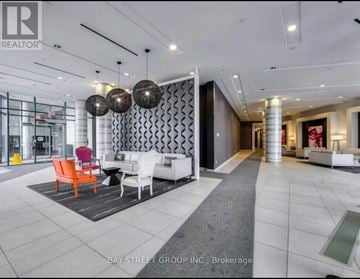 Toronto (Niagara) condo for rent - A spacious living room with a white sofa set and a patterned wallpaper.