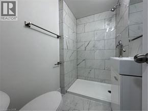 Kitchener apartment for rent - A white toilet sits next to a walk-in shower with a marble tile wall.