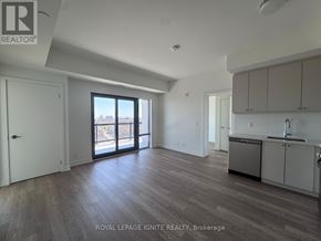 Clarington (Bowmanville) condo for rent - A spacious room with wooden flooring and a kitchen area with white cabinets.