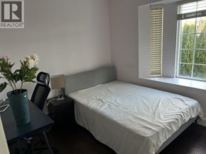 Burnaby apartment for rent - A bedroom with a bed, a table with a vase of flowers, and a window with blinds.