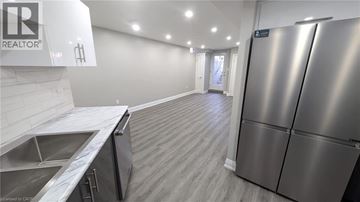 Hamilton apartment for rent - A stainless steel refrigerator is in a kitchen with a sink and wooden flooring.