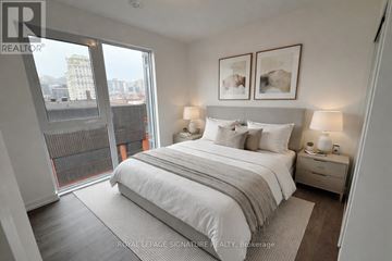Hamilton (Corktown) condo for rent - A bedroom with a large bed, two nightstands with lamps, and a view of the city through a large window.