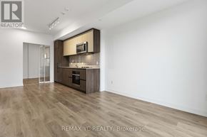 Toronto (South Riverdale) condo for rent - A spacious, empty room with wood flooring and a kitchenette area.