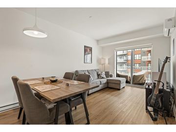 Gatineau (Aylmer) condo for rent - A modern living room with a wooden dining table and chairs, a couch, a guitar, and a window overlooking a building.