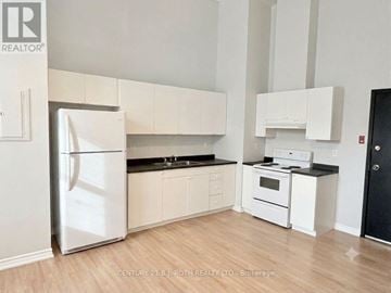 Barrie (City Centre) multi-family for rent - A white refrigerator stands in a kitchen with white cabinets and a black stove.