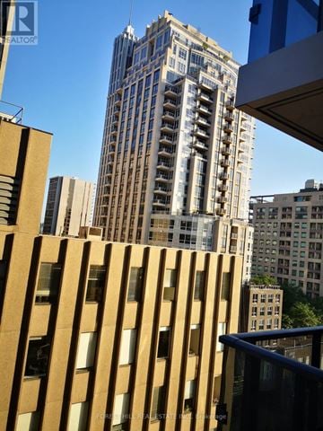 Toronto (Annex) condo for rent - A tall building with many windows stands in front of a blue sky.