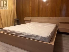 Vancouver apartment for rent - A bed with a white mattress and wooden headboard in a room with wooden walls.