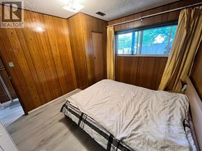 Vancouver apartment for rent - A bedroom with a bed, wooden walls, and a window with curtains.