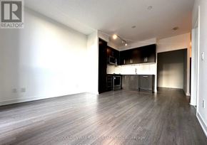 Toronto (Willowdale West) condo for rent - A spacious room with wooden flooring and a kitchen area in the background.