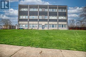 Fort Erie (Central) multi-family for rent - A large grey building with a green lawn in front.