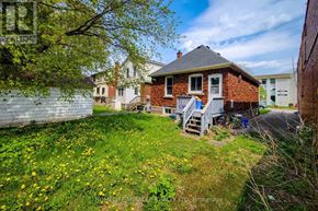 Hamilton (Westdale) apartment for rent - A house with a red brick exterior and a white door is surrounded by a grassy area with yellow flowers.