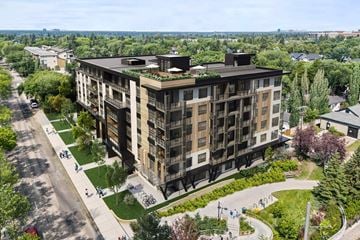 Edmonton apartment for rent - A large building with balconies and plants on the roof is surrounded by a green lawn and trees.