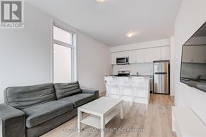 Oshawa (Samac) townhouse for rent - A grey couch sits in a white living room with a kitchen area in the background.