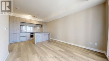 Richmond Hill condo for rent - A spacious room with wooden flooring and a kitchen area with a counter and cabinets.