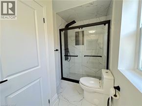Stoney Creek apartment for rent - A bathroom with a toilet, a glass shower door, and a cracked white tile floor.