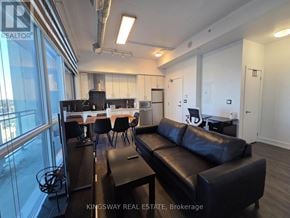 Toronto (Banbury-Don Mills) condo for rent - A black leather couch sits in a well-lit room with a kitchen area in the background.