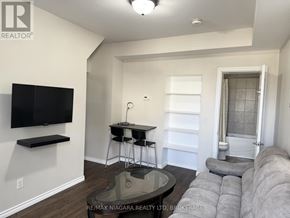 Niagara Falls (Downtown) duplex for rent - A living room with a grey couch and a black television mounted on the wall.