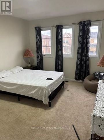 Oshawa (Taunton) apartment for rent - A bedroom with a bed, a window with curtains, and a lamp on a side table.