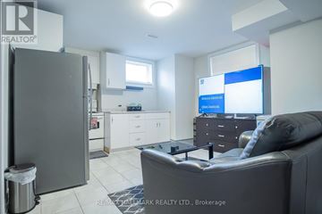 Toronto (Englemount-Lawrence) apartment for rent - A modern living room with a grey couch and a kitchen area in the background.
