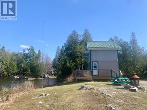 Kawartha Lakes (Verulam) apartment for rent - A house with a green roof is surrounded by trees and a body of water.