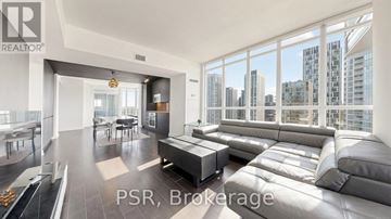 Toronto (Waterfront Communities) condo for rent - A modern living room with a large grey sofa and a view of the city.