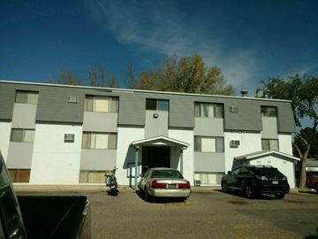 Pueblo apartment for rent - A grey building with a car parked in front.