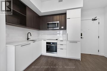 Toronto (Dovercourt-Wallace Emerson-Junction) condo for rent - A modern kitchen with white cabinets and a wooden backsplash.