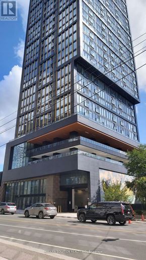 Toronto (Waterfront Communities) condo for rent - A tall building with a glass facade and a brown base is surrounded by parked cars.