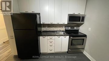 Welland (Welland Downtown) townhouse for rent - A black refrigerator and stove in a kitchen with white cabinets.