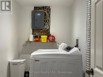 Mississauga (Malton) apartment for rent - A small white washing machine sits in a room with a wall-mounted dryer and a white trash can.