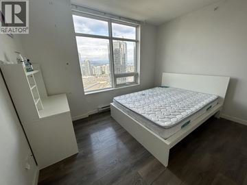 Burnaby apartment for rent - A bedroom with a large bed and a window overlooking a cityscape.