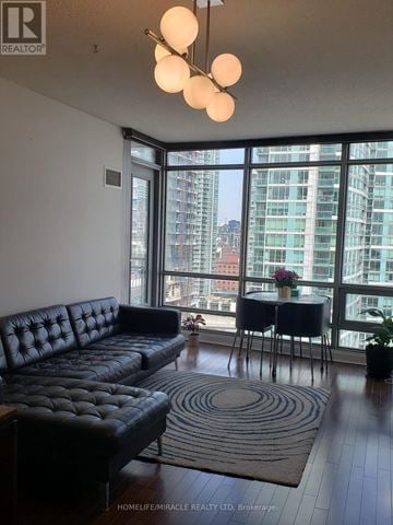 Toronto (Waterfront Communities) condo for rent - A living room with a black couch and a round table with a vase of flowers on it.