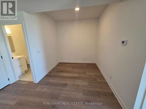 Brantford condo for rent - A room with wooden flooring and white walls, with a kitchen visible in the background.