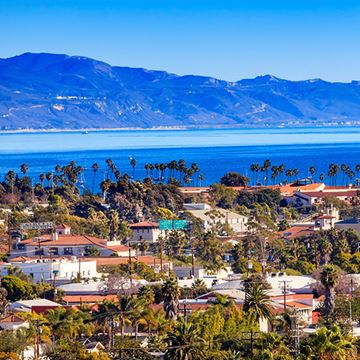 Toronto apartment for rent - A coastal town with houses and palm trees in the foreground and mountains in the background.