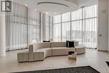 Burlington (Alton) condo for rent - A modern living room with a curved sofa and a large window.
