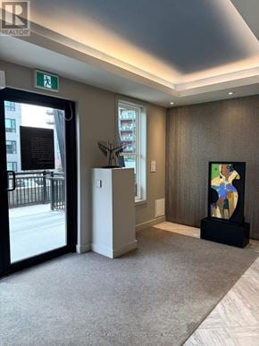 Barrie (400 West) condo for rent - A hallway with a carpeted floor, a door with a window, a plant, and a painting on the wall.