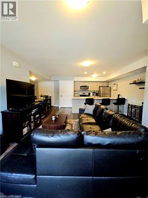 Kitchener townhouse for rent - A black leather couch sits in a living room with a television and a kitchen area in the background.