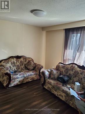 Mississauga (Malton) apartment for rent - A realtor is showing a living room with two floral patterned couches.