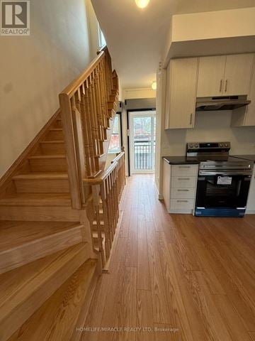 Aurora (Aurora Village) townhouse for rent - A wooden staircase leads to a kitchen area with white cabinets and a black oven.