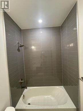 Kitchener condo for rent - A small white bathtub in a bathroom with grey tiles.