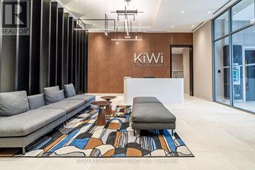 Hamilton (Beasley) condo for rent - A modern living room with a grey sofa and a wooden wall with the words Kiwi Condo Infiniums on it.