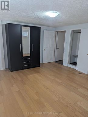 Brampton (Huttonville) apartment for rent - A black wardrobe with a mirror door is in the middle of a room with wooden flooring.