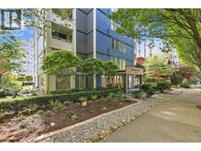 Vancouver apartment for rent - A modern building with a blue and beige facade surrounded by greenery and a gravel path.