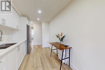 Toronto (Mimico) triplex for rent - A kitchen with white cabinets and a wooden table with a vase of flowers on it.