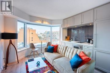 Toronto (Annex) condo for rent - A living room with a couch, a rug, a floor lamp and a window overlooking the city.