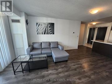 Toronto (Willowdale East) condo for rent - A living room with a grey couch and a glass coffee table.