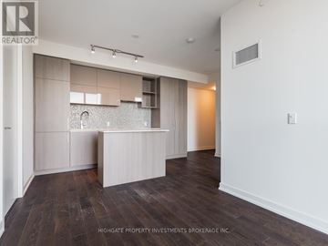 Toronto (Annex) condo for rent - A spacious room with wooden flooring and a kitchen area with a sink and cabinets.