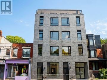 Toronto (Annex) multi-family for rent - A tall grey building with many windows is in the middle of a street.