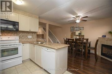 Brampton (Central Park) townhouse for rent - A kitchen with white appliances and cabinets, a dining table with chairs, and a fireplace.